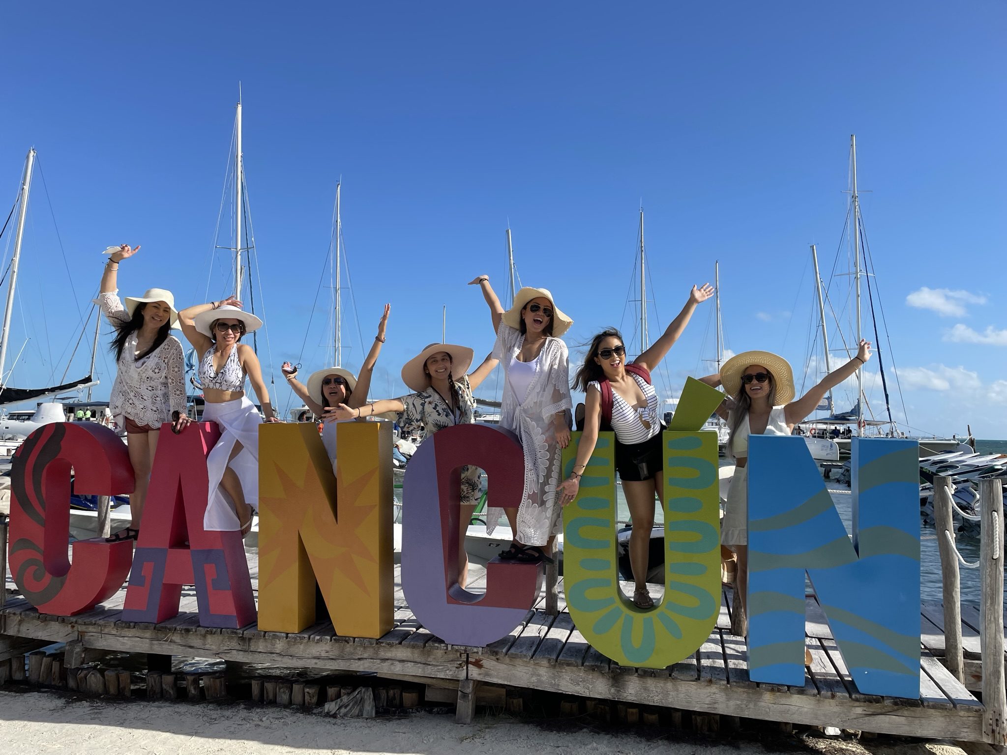 People posing with colorful Cancun sign, boats background.
